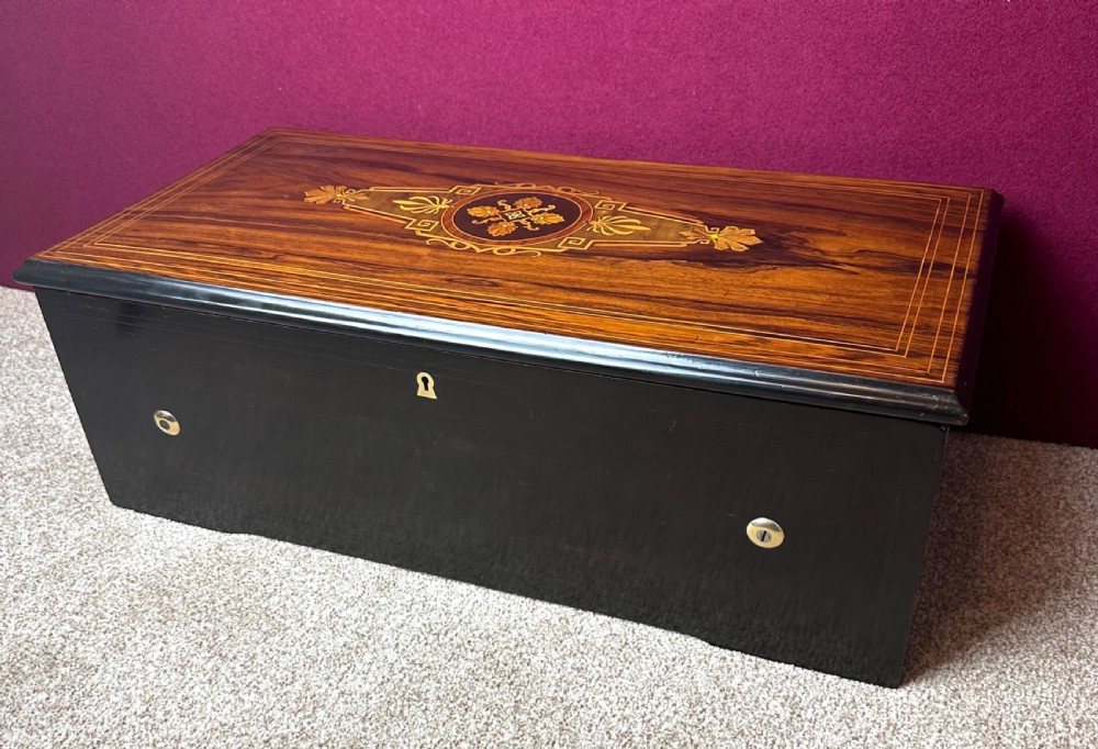 A rectangular Victorian ebonised wooden music box with an inlaid marquetry top featuring foliage motifs and a brass keyhole escutcheon.