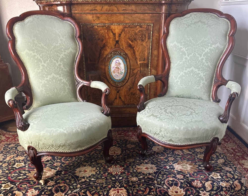 A pair of late Victorian carved mahogany salon armchairs upholstered in light green damask fabric featuring cabriole legs and scroll arms.
