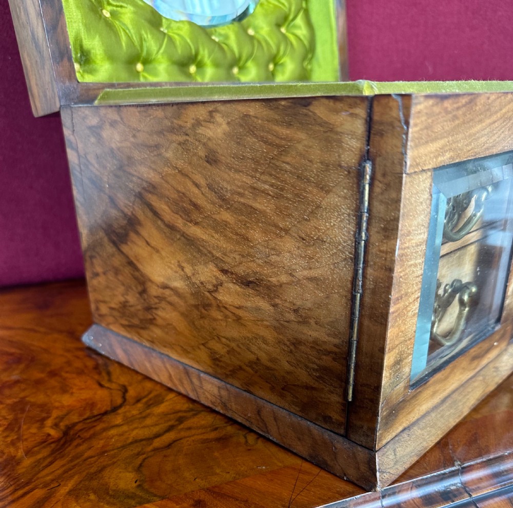 An open Victorian walnut sewing box with a green tufted silk interior lid, an inset mirror, and four small drawers with brass drop handles on the front. View III