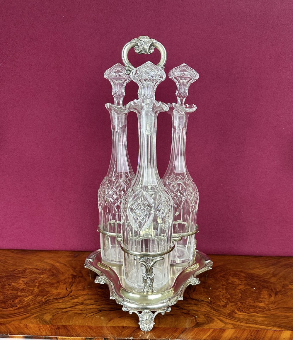 A Victorian silver-plated trefoil frame containing three tall cut-glass decanters with matching faceted glass stoppers.