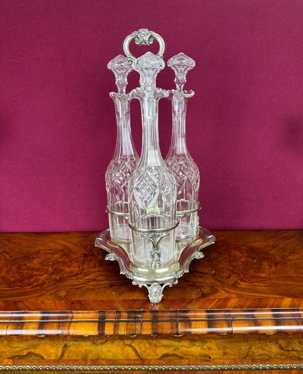 A Victorian silver-plated trefoil frame containing three tall cut-glass decanters with matching faceted glass stoppers. View VII