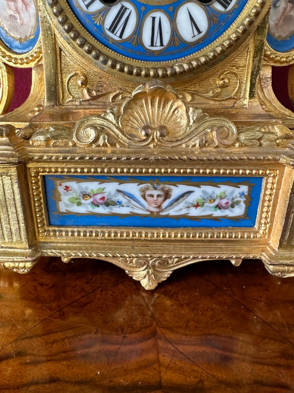 A French Rococo Revival gilt bronze mantel clock surmounted by a sculpted cherub, featuring blue porcelain panels and an enamel Roman numeral dial. View VIII