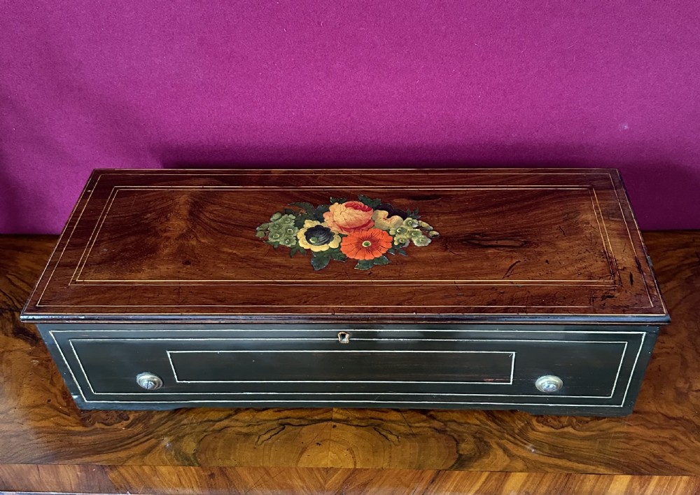 A Victorian rosewood cylinder music box featuring central floral marquetry inlay and an ebonised case with line stringing.