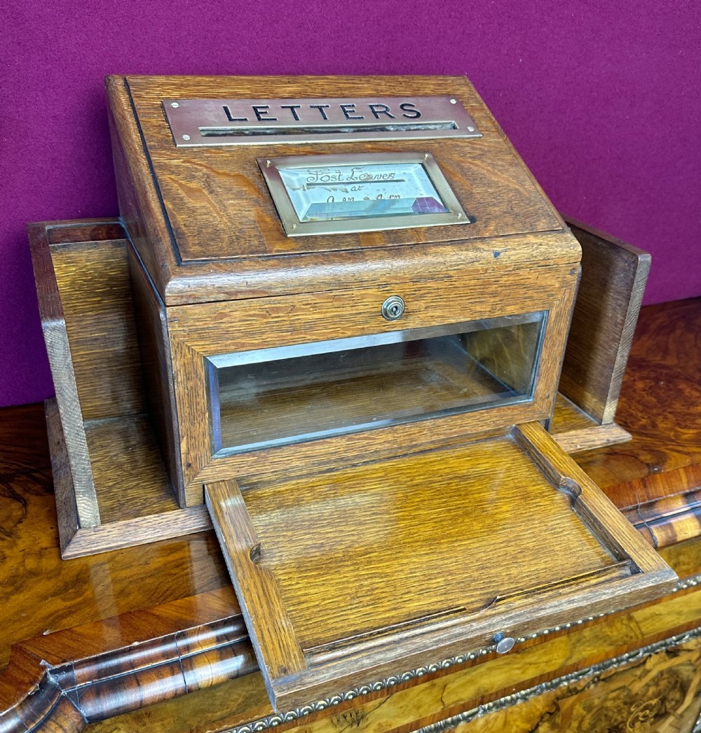 An Edwardian oak tabletop letter box featuring a slanted top with a brass aperture marked LETTERS, a collection schedule window, a glass front panel, and side stationery slots. View II
