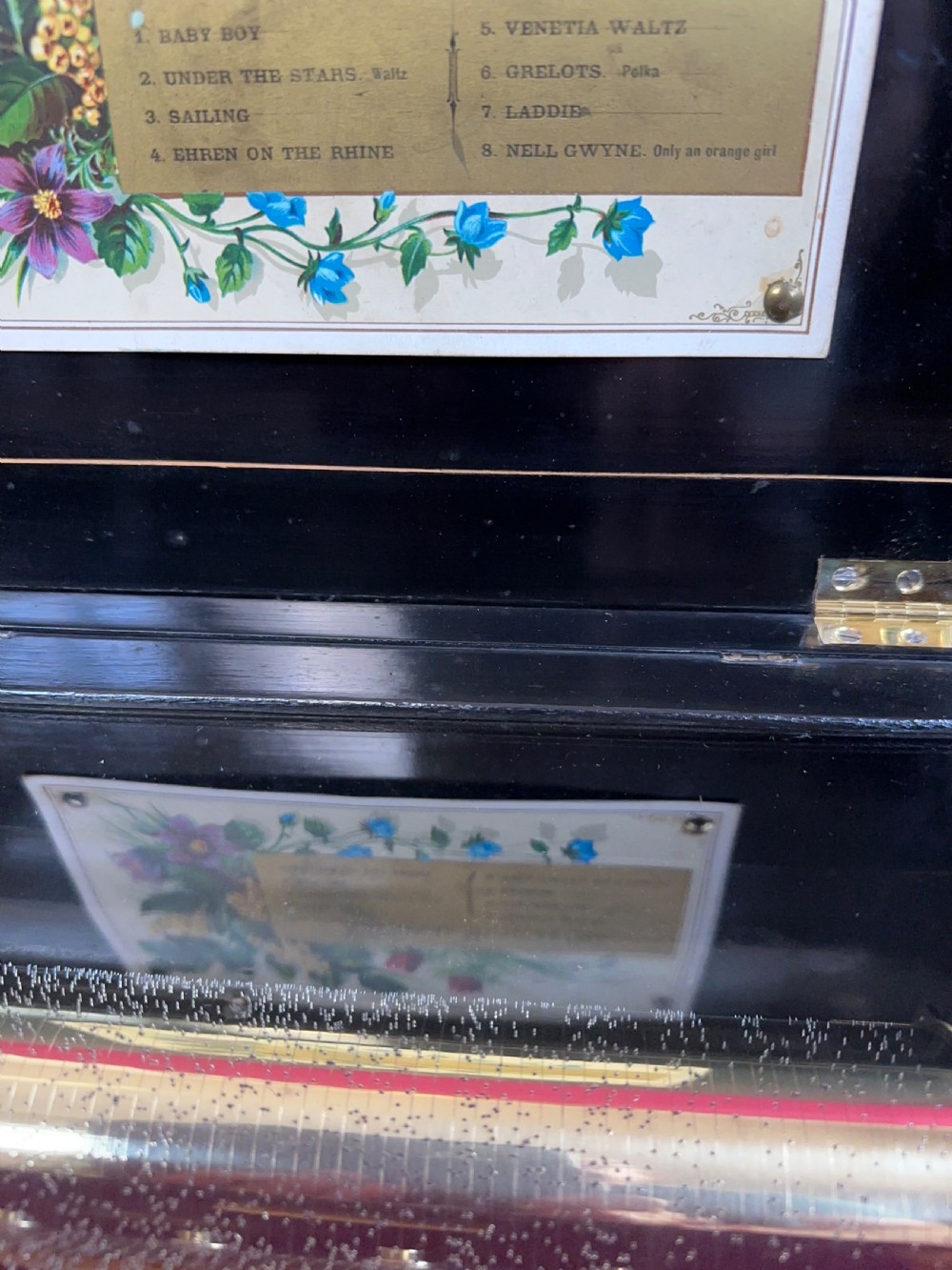 An antique Victorian ebonised wood musical box shown open, displaying its brass cylinder mechanism and an illustrated paper tune card. View IV