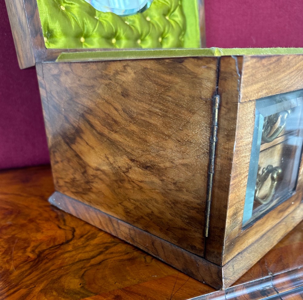 An open late Victorian walnut jewellery and sewing box featuring a green tufted silk lid lining with an oval mirror, top storage section, and two lower drawers behind glass doors. View II