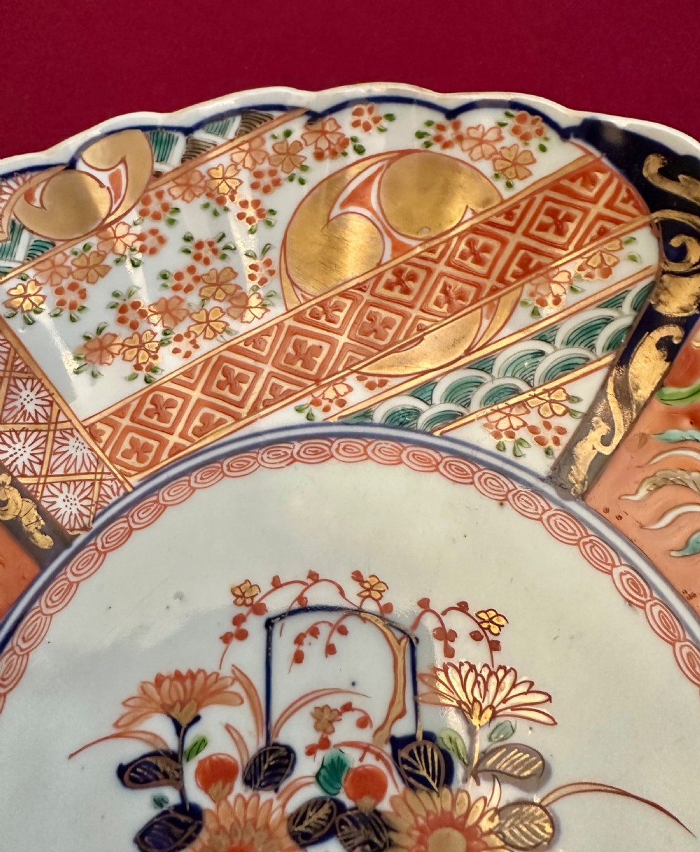 A pair of circular Japanese Imari porcelain chargers featuring scalloped edges, cobalt blue and iron-red painted panels, and central flower basket motifs with gilded accents. View VI