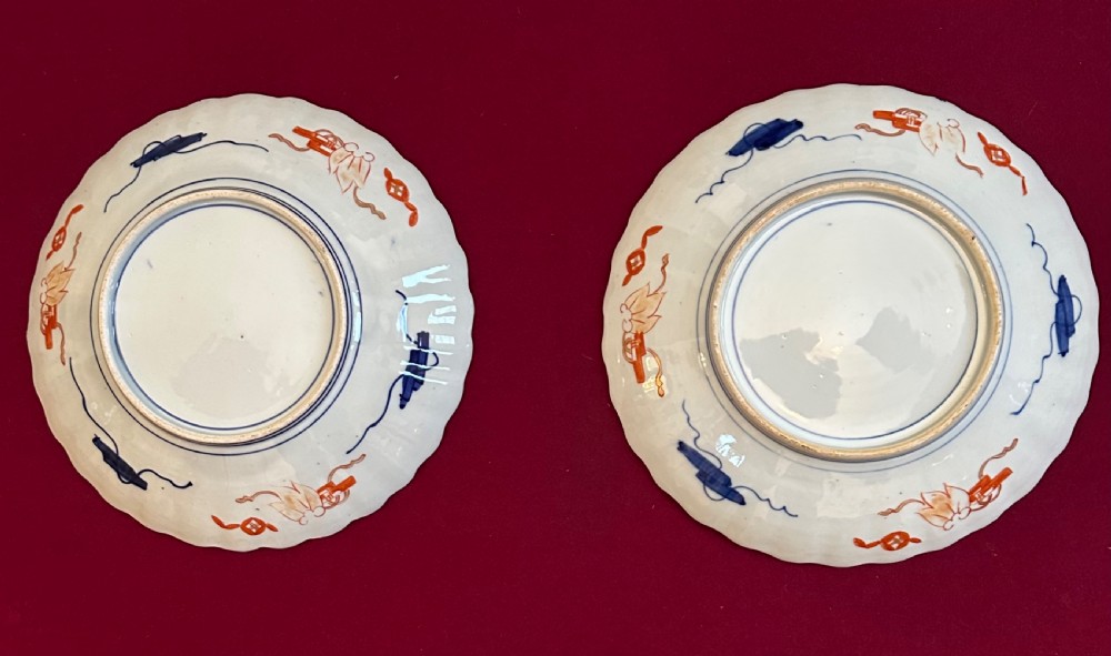 A pair of circular Japanese Imari porcelain chargers featuring scalloped edges, cobalt blue and iron-red painted panels, and central flower basket motifs with gilded accents. View VIII
