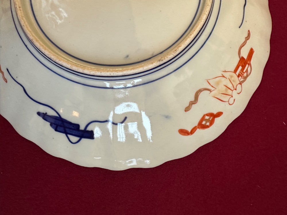 A pair of circular Japanese Imari porcelain chargers featuring scalloped edges, cobalt blue and iron-red painted panels, and central flower basket motifs with gilded accents. View IX