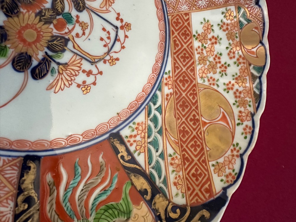 A pair of circular Japanese Imari porcelain chargers featuring scalloped edges, cobalt blue and iron-red painted panels, and central flower basket motifs with gilded accents. View X