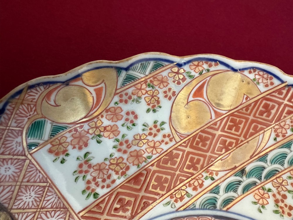 A pair of circular Japanese Imari porcelain chargers featuring scalloped edges, cobalt blue and iron-red painted panels, and central flower basket motifs with gilded accents. View XI