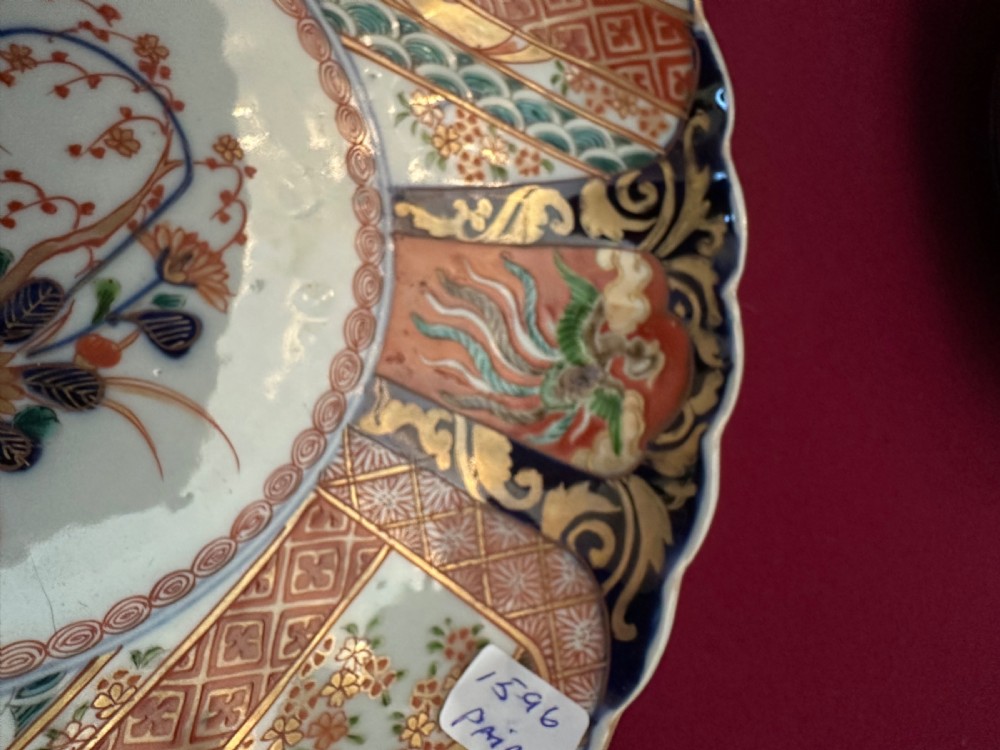 A pair of circular Japanese Imari porcelain chargers featuring scalloped edges, cobalt blue and iron-red painted panels, and central flower basket motifs with gilded accents. View XII
