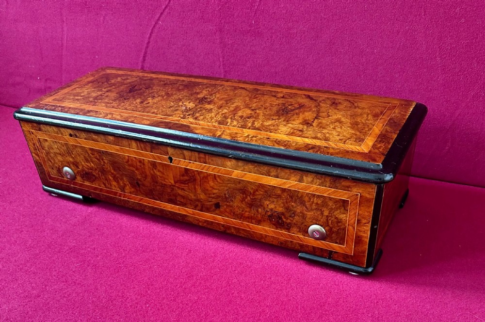 A rectangular Victorian burr walnut cylinder music box featuring ebonised borders and boxwood inlay stringing.