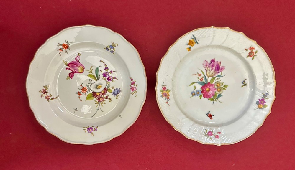 A pair of round white porcelain plates featuring hand-painted botanical flowers with scalloped edges.