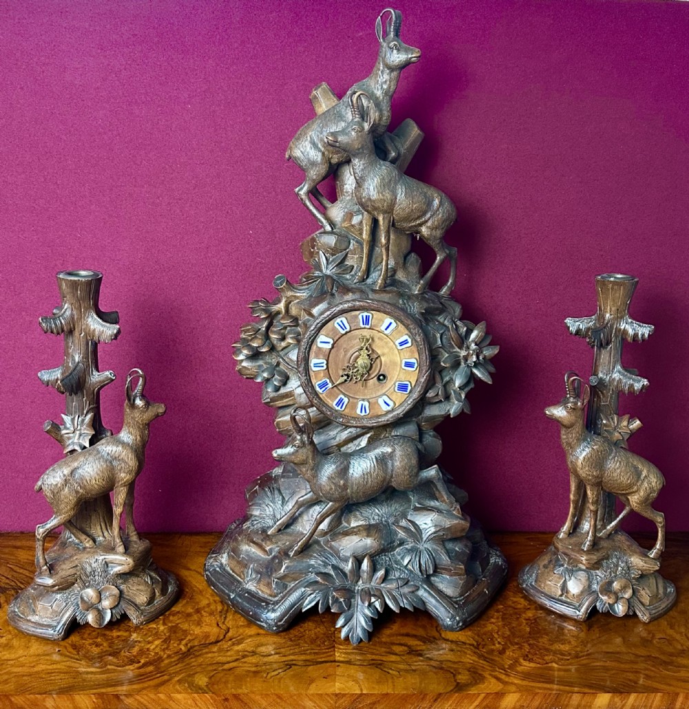A three-piece carved wooden Black Forest clock garniture set featuring alpine chamois figures mounted among carved foliage and tree trunks around a central clock dial.