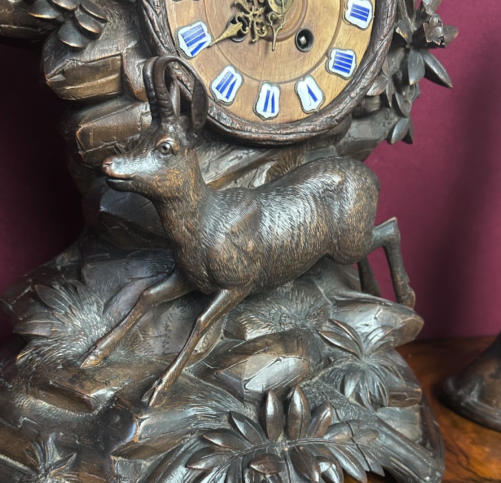 A three-piece carved wooden Black Forest clock garniture set featuring alpine chamois figures mounted among carved foliage and tree trunks around a central clock dial. View VII