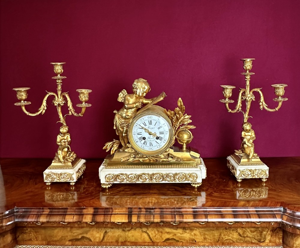 A 19th-century French gilt bronze and white marble clock garniture set comprising a central clock with a cherub motif and two flanking three-light candelabras.