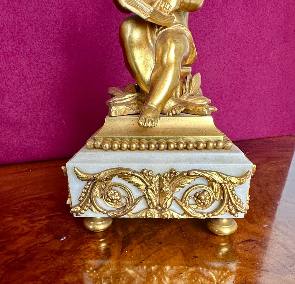 A 19th-century French gilt bronze and white marble clock garniture set comprising a central clock with a cherub motif and two flanking three-light candelabras. View VIII