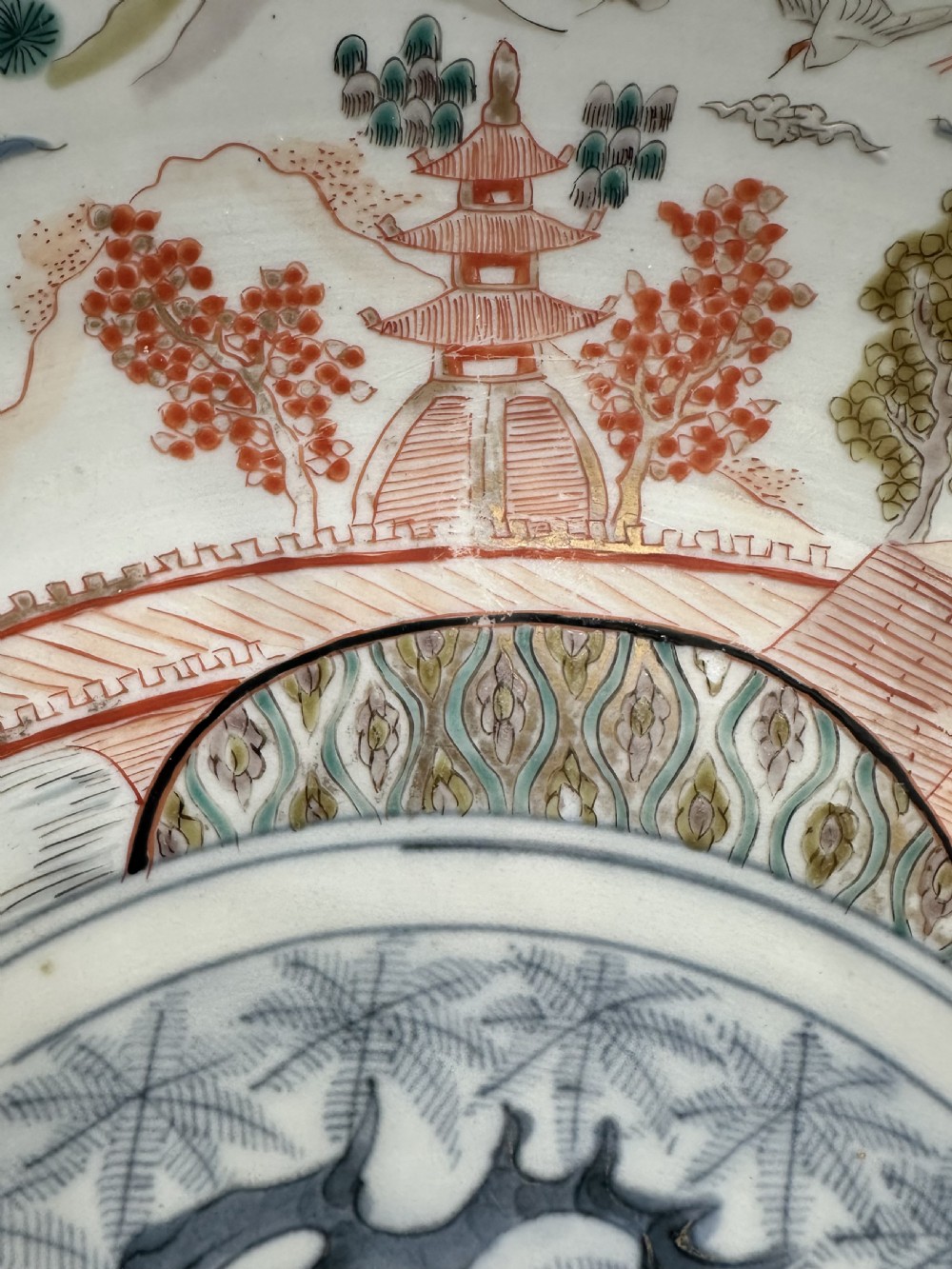 A large circular Japanese Imari porcelain charger decorated with underglaze cobalt blue and overglaze terracotta red enamels depicting landscape scenes and geometric borders. View VI