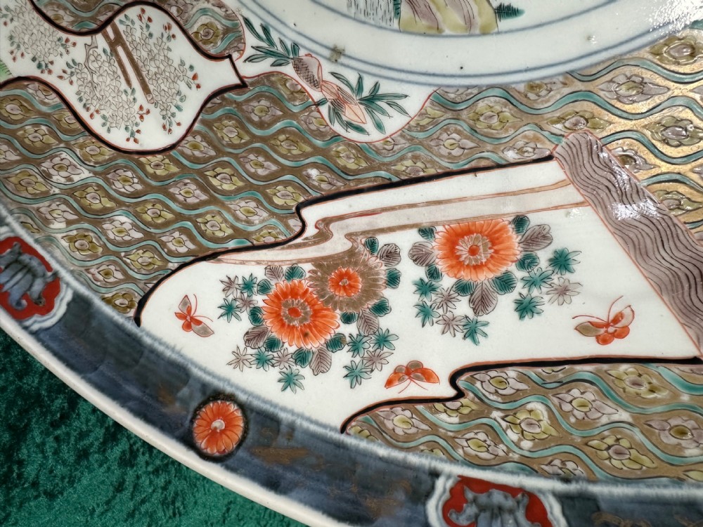 A large circular Japanese Imari porcelain charger decorated with underglaze cobalt blue and overglaze terracotta red enamels depicting landscape scenes and geometric borders. View VII