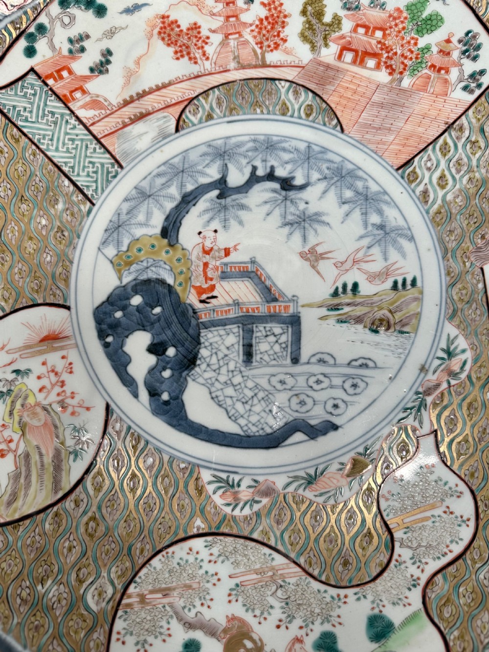 A large circular Japanese Imari porcelain charger decorated with underglaze cobalt blue and overglaze terracotta red enamels depicting landscape scenes and geometric borders. View VIII