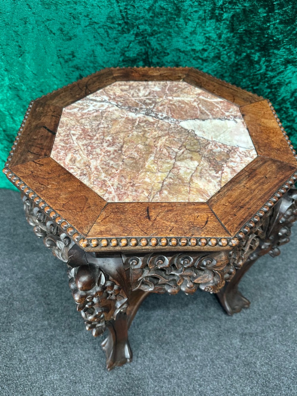 A dark carved padouk wood hexagonal stand featuring an inset marble top, pierced foliage apron, and cabriole legs. View II