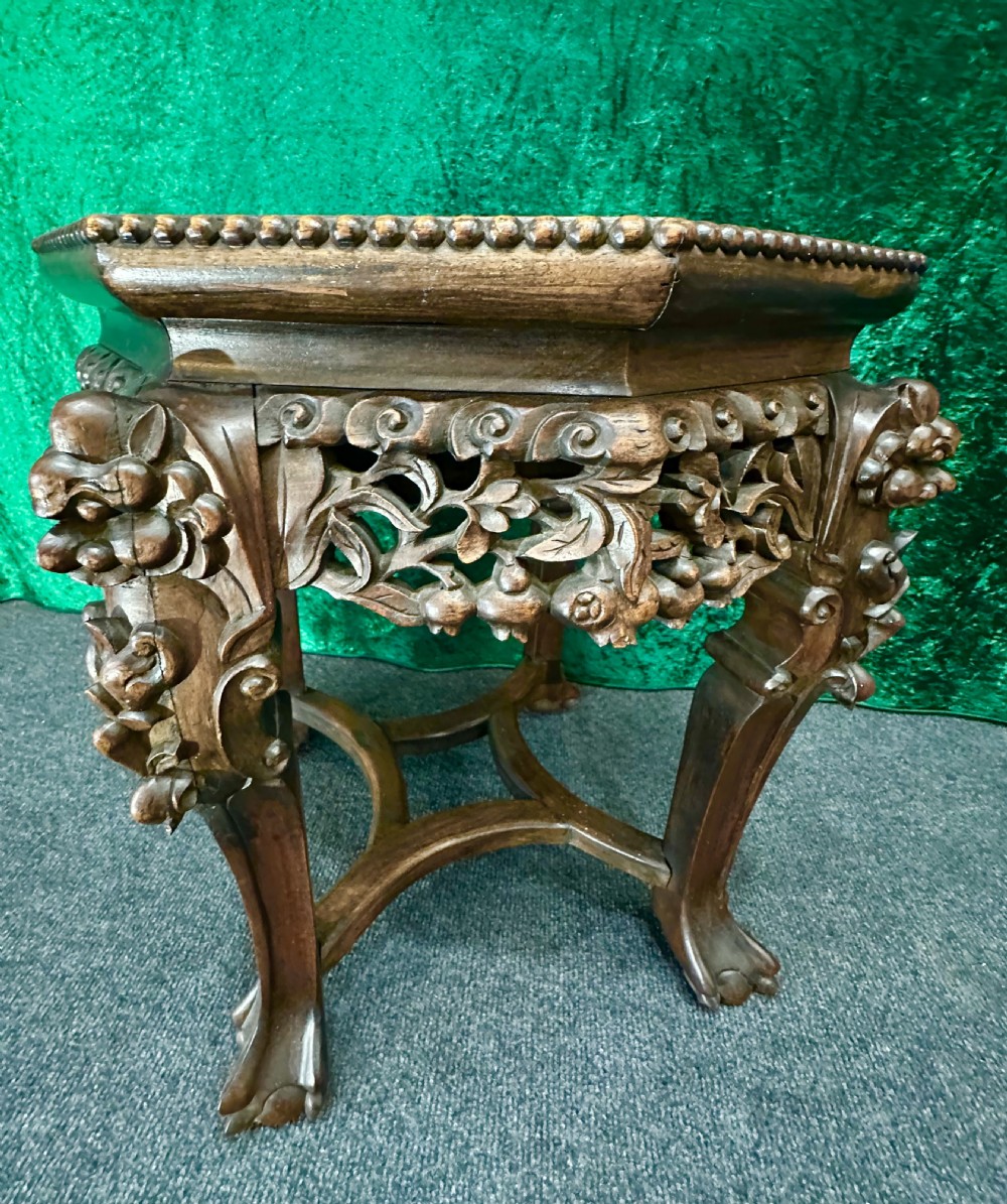 A dark carved padouk wood hexagonal stand featuring an inset marble top, pierced foliage apron, and cabriole legs. View III