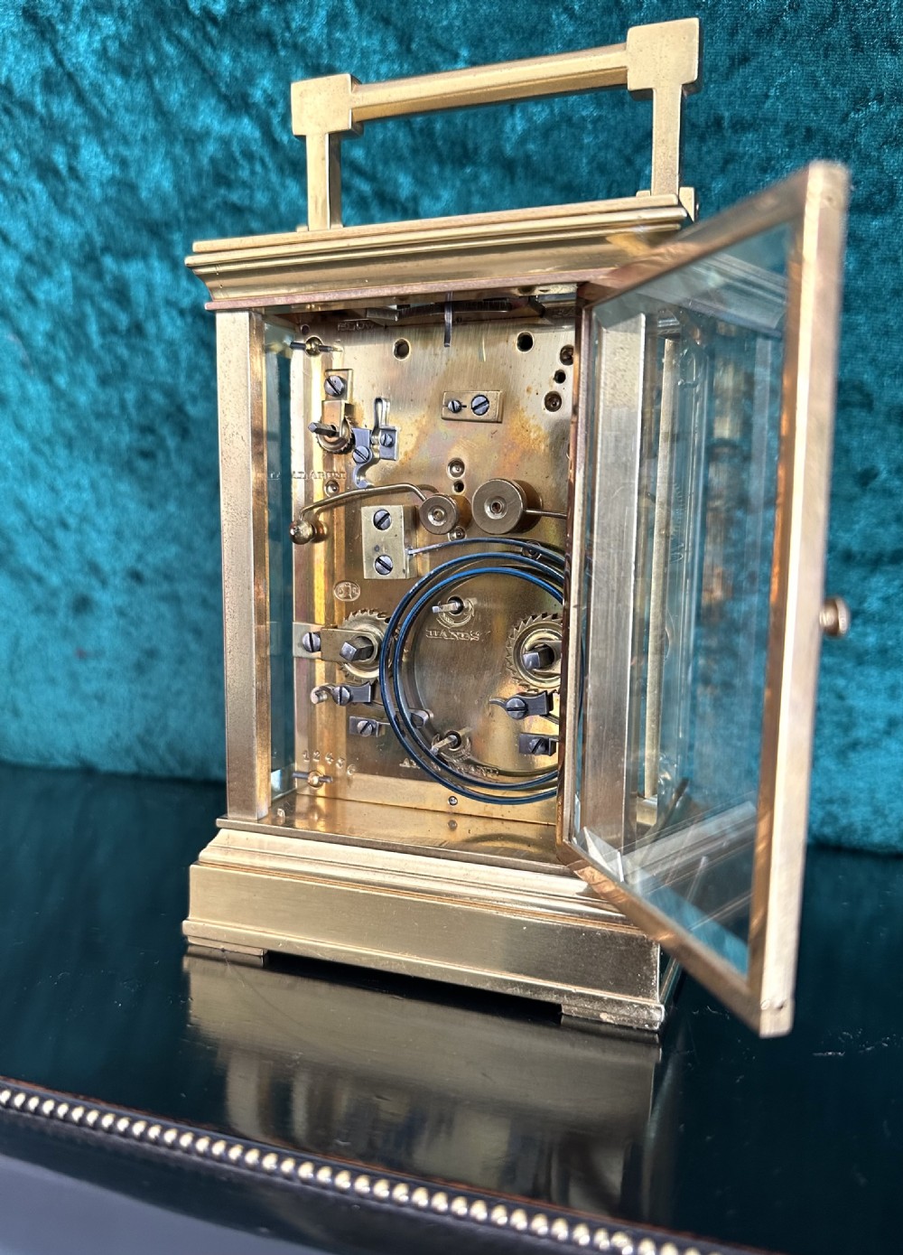 A late 19th-century gilt brass French carriage clock featuring a rectangular case, top carrying handle, glass panels revealing internal gears, and a white enamel dial with Roman numerals. View VI