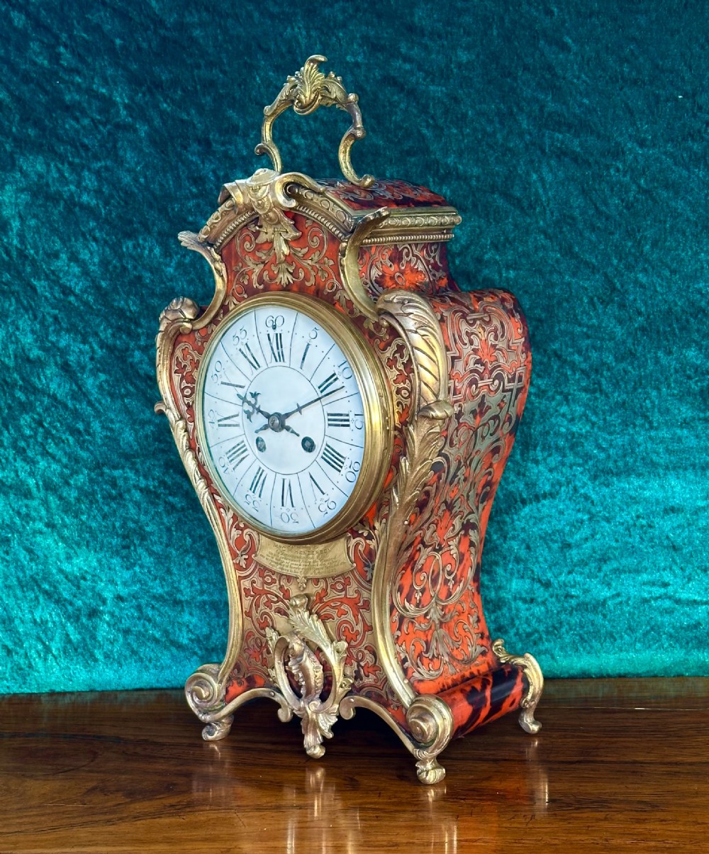 A 19th-century French Louis XV style Boulle mantel clock featuring red tortoiseshell and brass marquetry inlay with gilt bronze mounts.