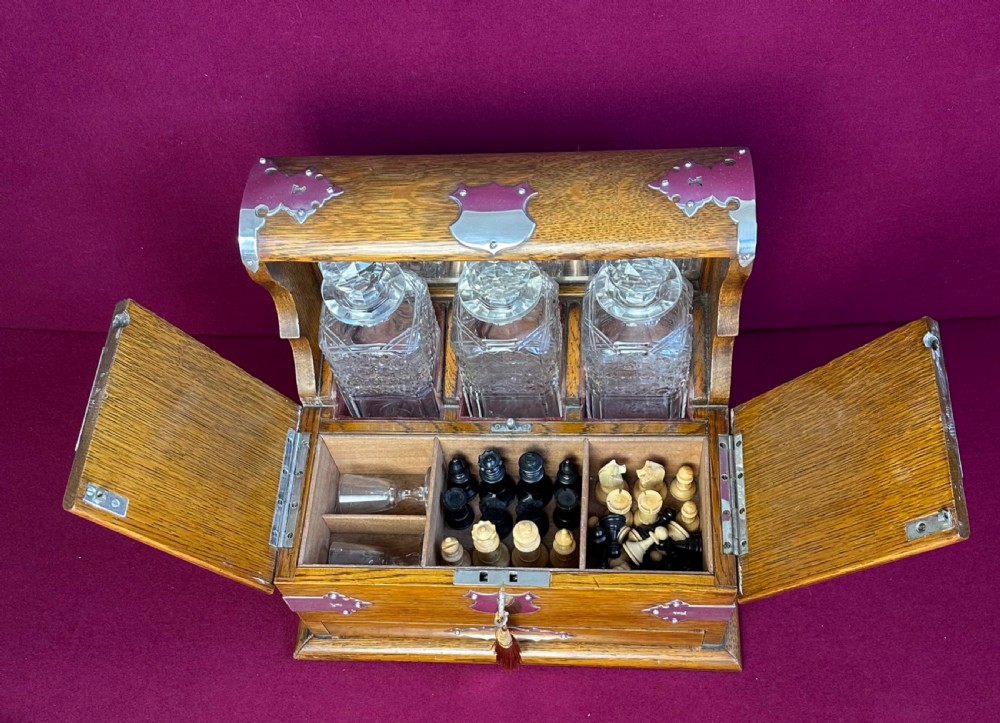 An open Edwardian oak games compendium displaying three cut crystal decanters, chess pieces, cribbage board, dominoes, and playing cards. View VIII