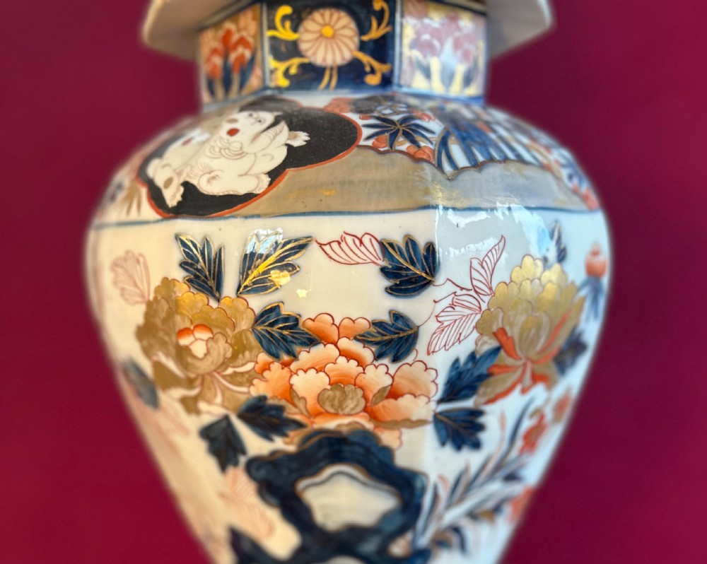 An octagonal porcelain covered vase decorated in Japanese Imari style with floral motifs and topped with a sculpted red foo dog finial. View II