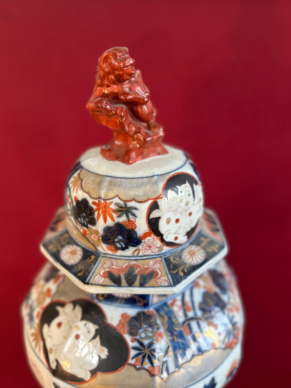 An octagonal porcelain covered vase decorated in Japanese Imari style with floral motifs and topped with a sculpted red foo dog finial. View III