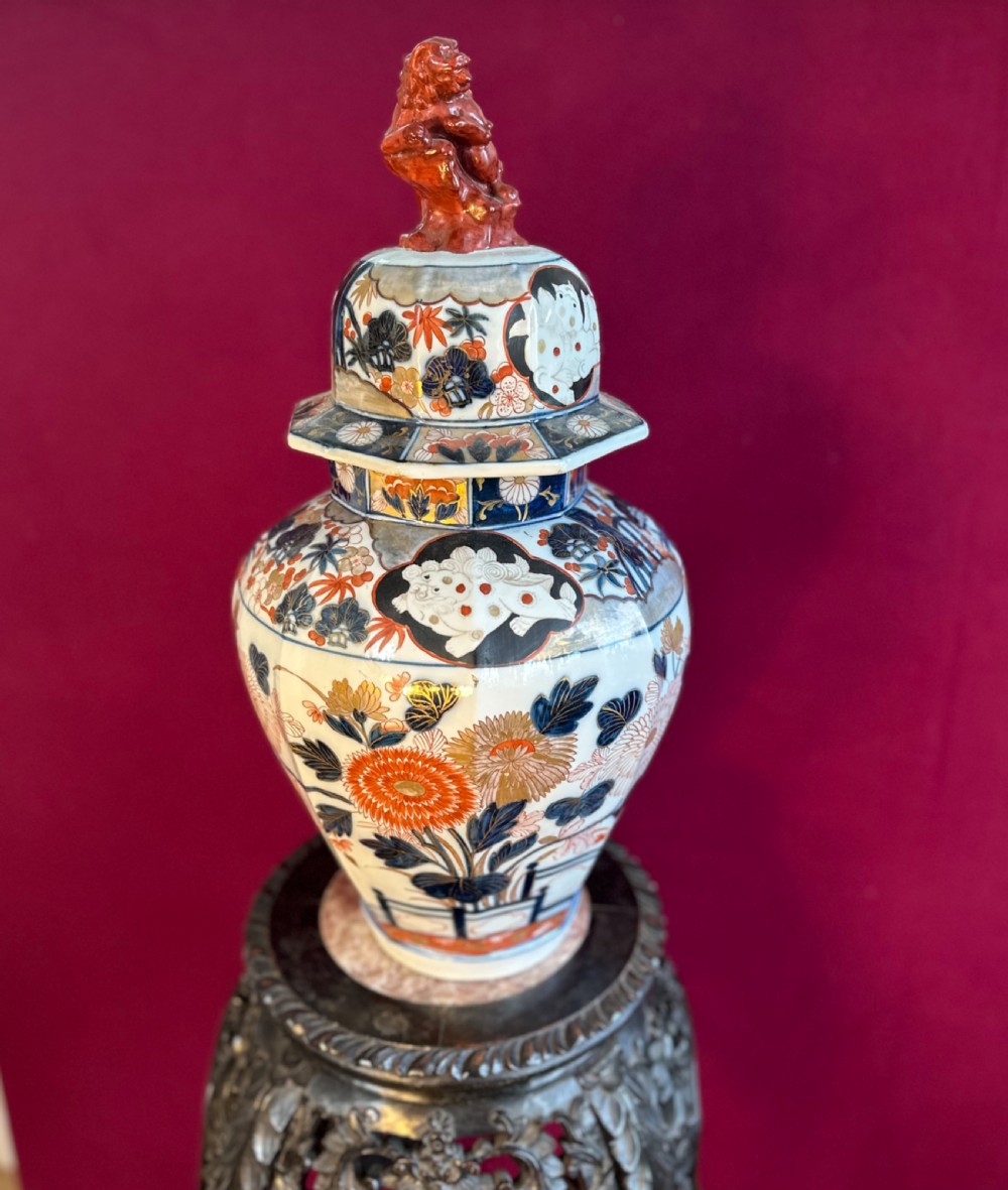An octagonal porcelain covered vase decorated in Japanese Imari style with floral motifs and topped with a sculpted red foo dog finial. View V