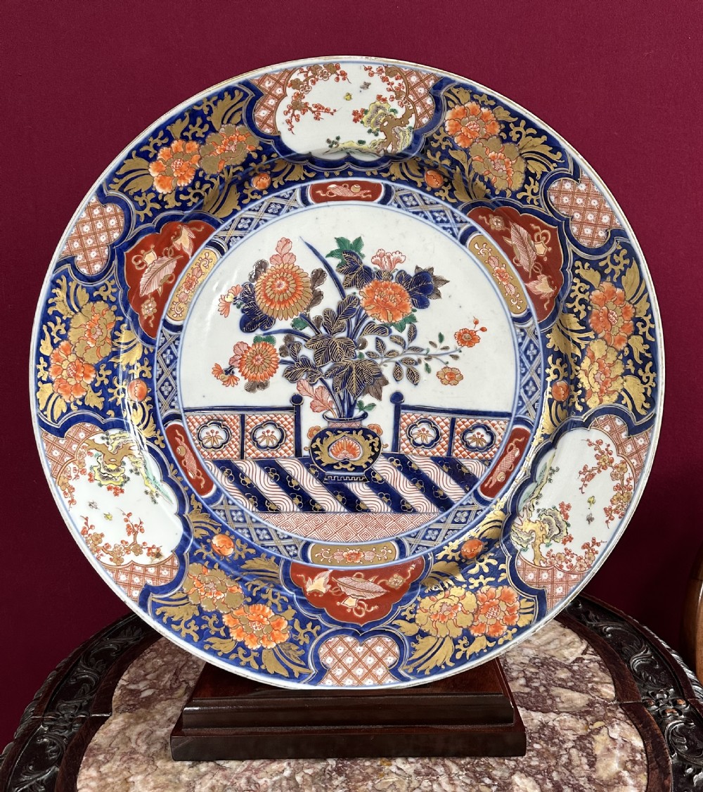 A circular Japanese Imari porcelain charger decorated with cobalt blue, iron red, and orange floral motifs around a central urn pattern. View V