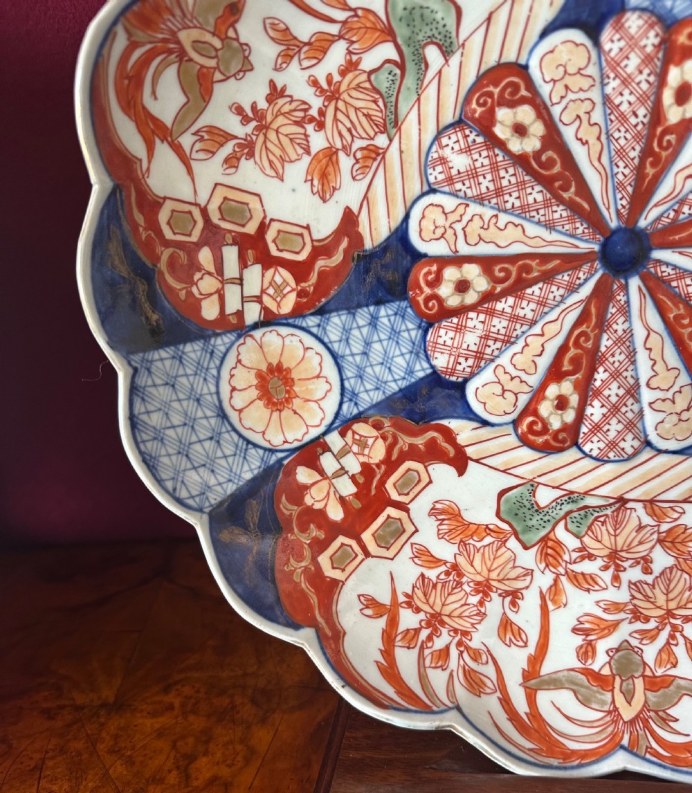 A pair of circular Japanese Imari porcelain chargers with scalloped edges, featuring intricate floral panels in cobalt blue, rust red, and white. View III