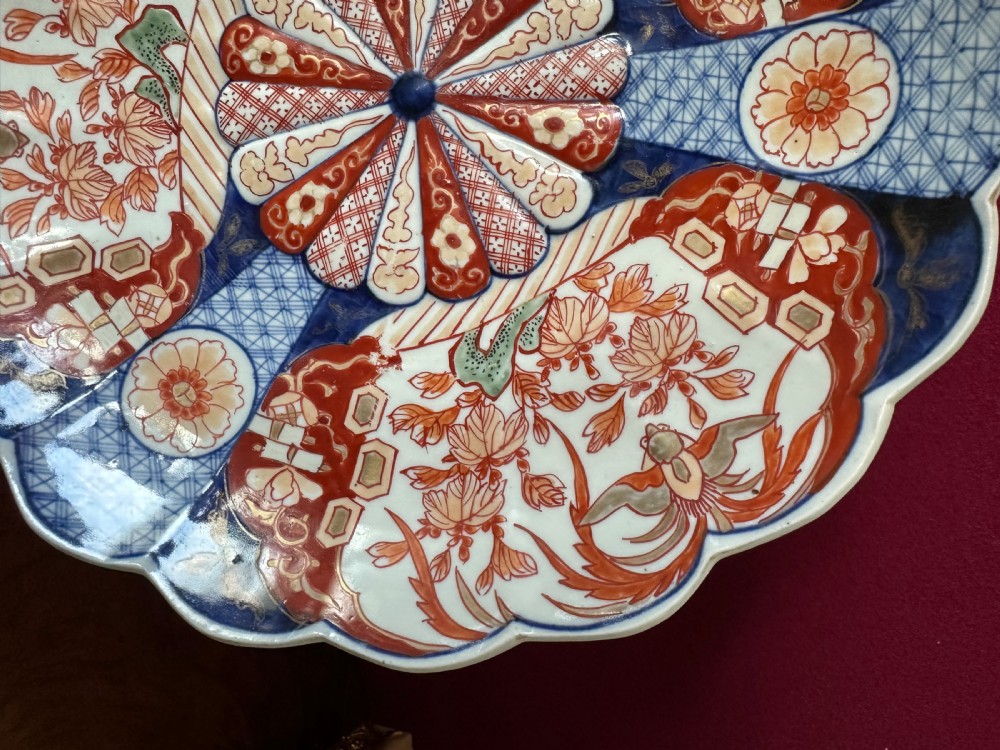 A pair of circular Japanese Imari porcelain chargers with scalloped edges, featuring intricate floral panels in cobalt blue, rust red, and white. View V