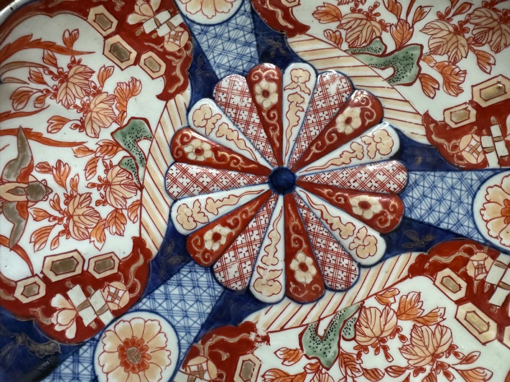 A pair of circular Japanese Imari porcelain chargers with scalloped edges, featuring intricate floral panels in cobalt blue, rust red, and white. View VI