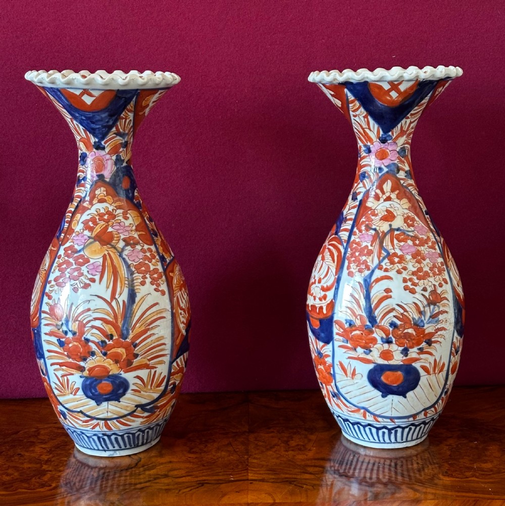 A pair of baluster-shaped Japanese Imari porcelain vases decorated with floral panels in cobalt blue and rust red, featuring crimped scalloped rims.