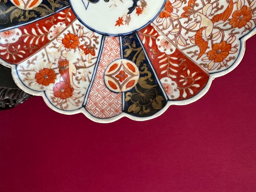 A circular Japanese Imari porcelain charger plate featuring a scalloped edge, central floral motif, and alternating radiated panels of iron-red floral patterns and navy blue gilt detailing. View III