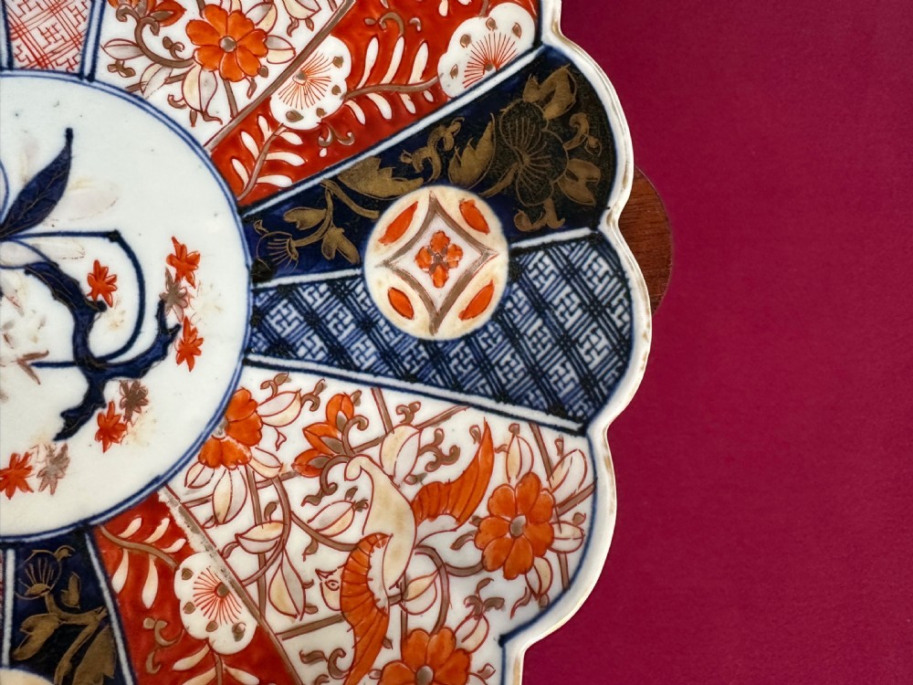 A circular Japanese Imari porcelain charger plate featuring a scalloped edge, central floral motif, and alternating radiated panels of iron-red floral patterns and navy blue gilt detailing. View V