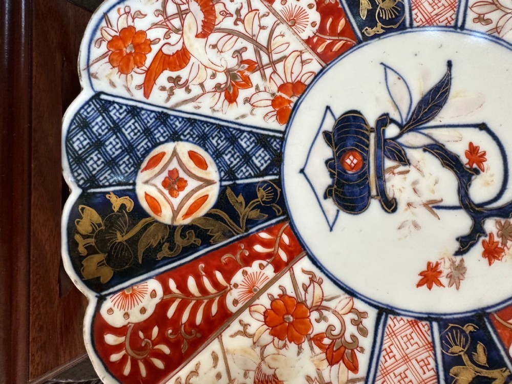 A circular Japanese Imari porcelain charger plate featuring a scalloped edge, central floral motif, and alternating radiated panels of iron-red floral patterns and navy blue gilt detailing. View VII
