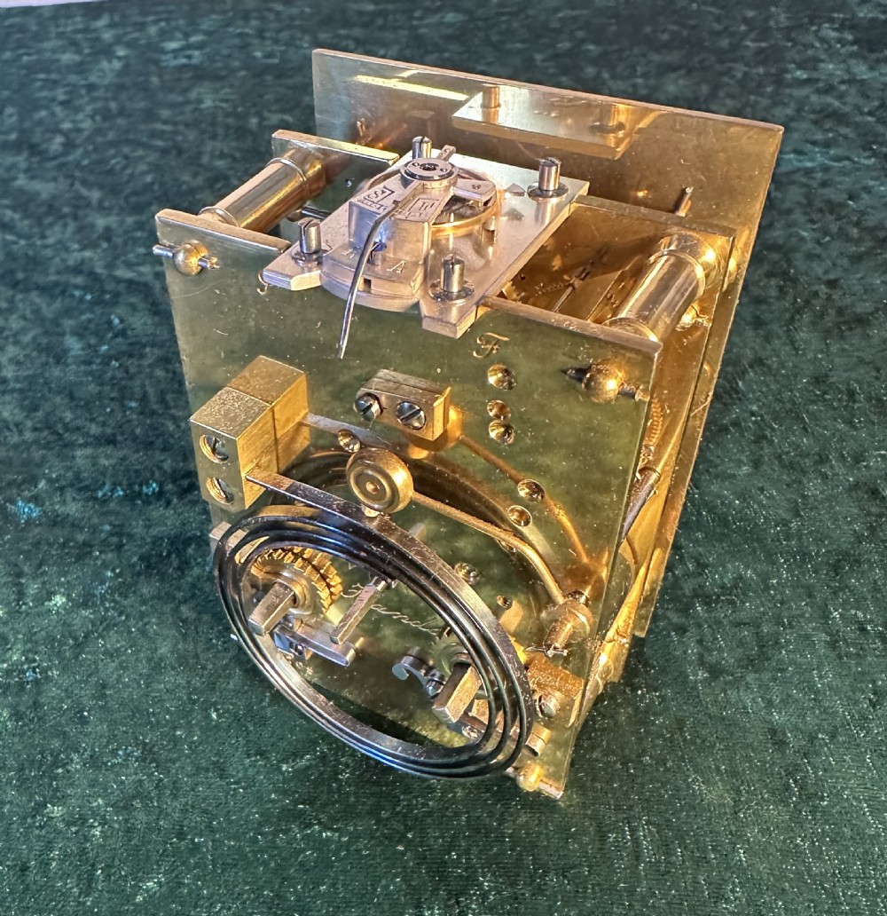 A rectangular brass carriage clock featuring glass side panels, a white enamel dial with black Roman numerals, and a top carrying handle. View VII