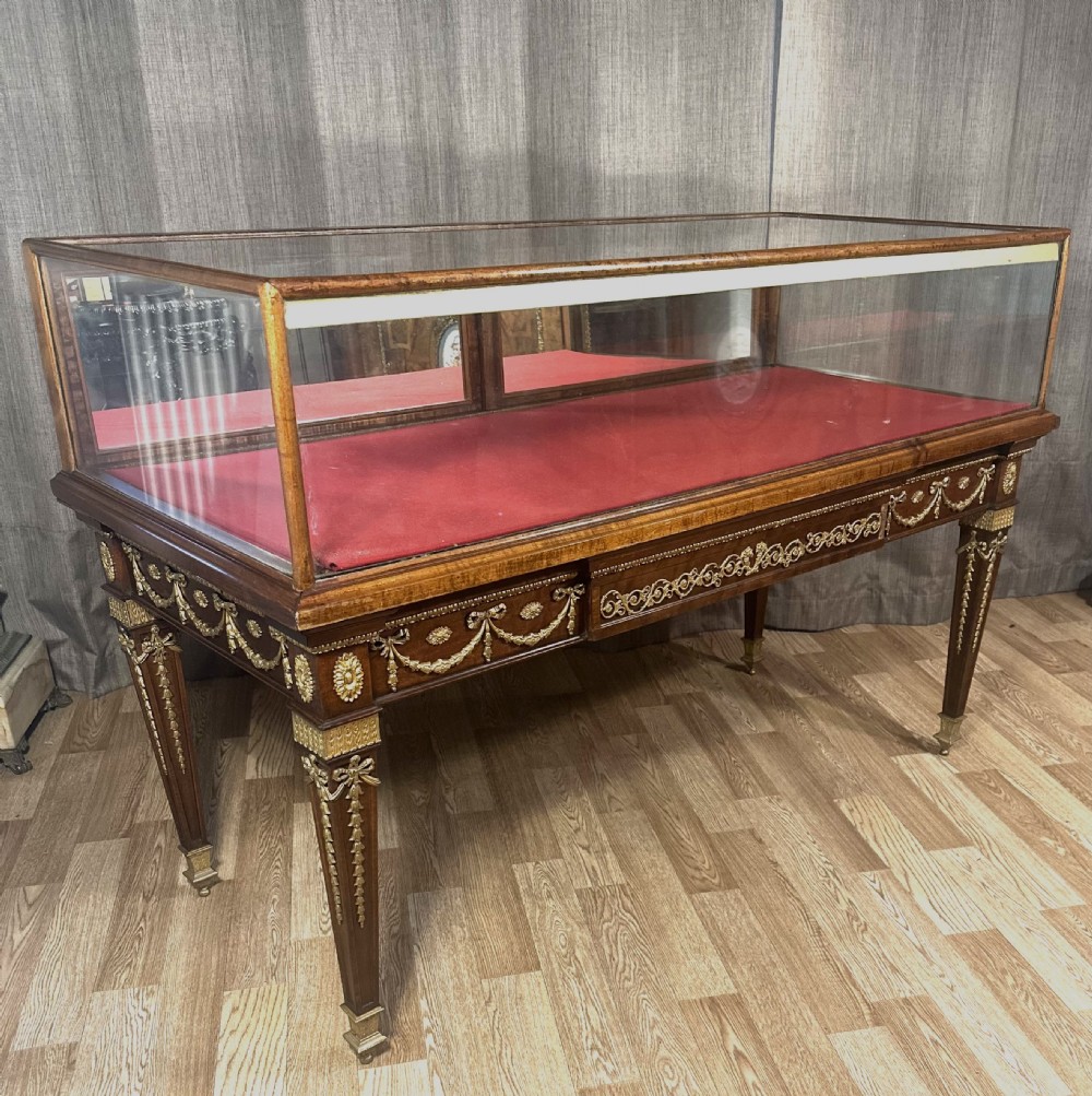 A late 19th-century mahogany table vitrine featuring clear glass panels, a red velvet interior base, tapered legs, and decorative gilt-bronze mounts.