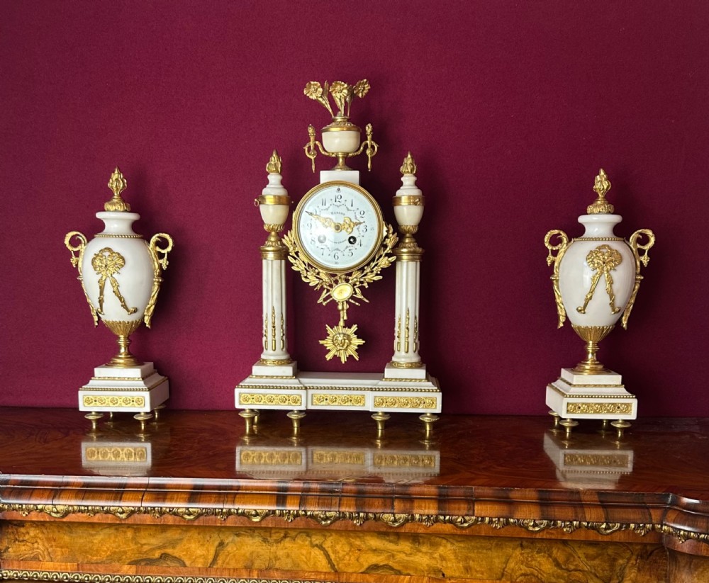 A late 19th-century French three-piece garniture set featuring a central white marble and gilt-bronze portico clock flanked by two matching ornamental urns.