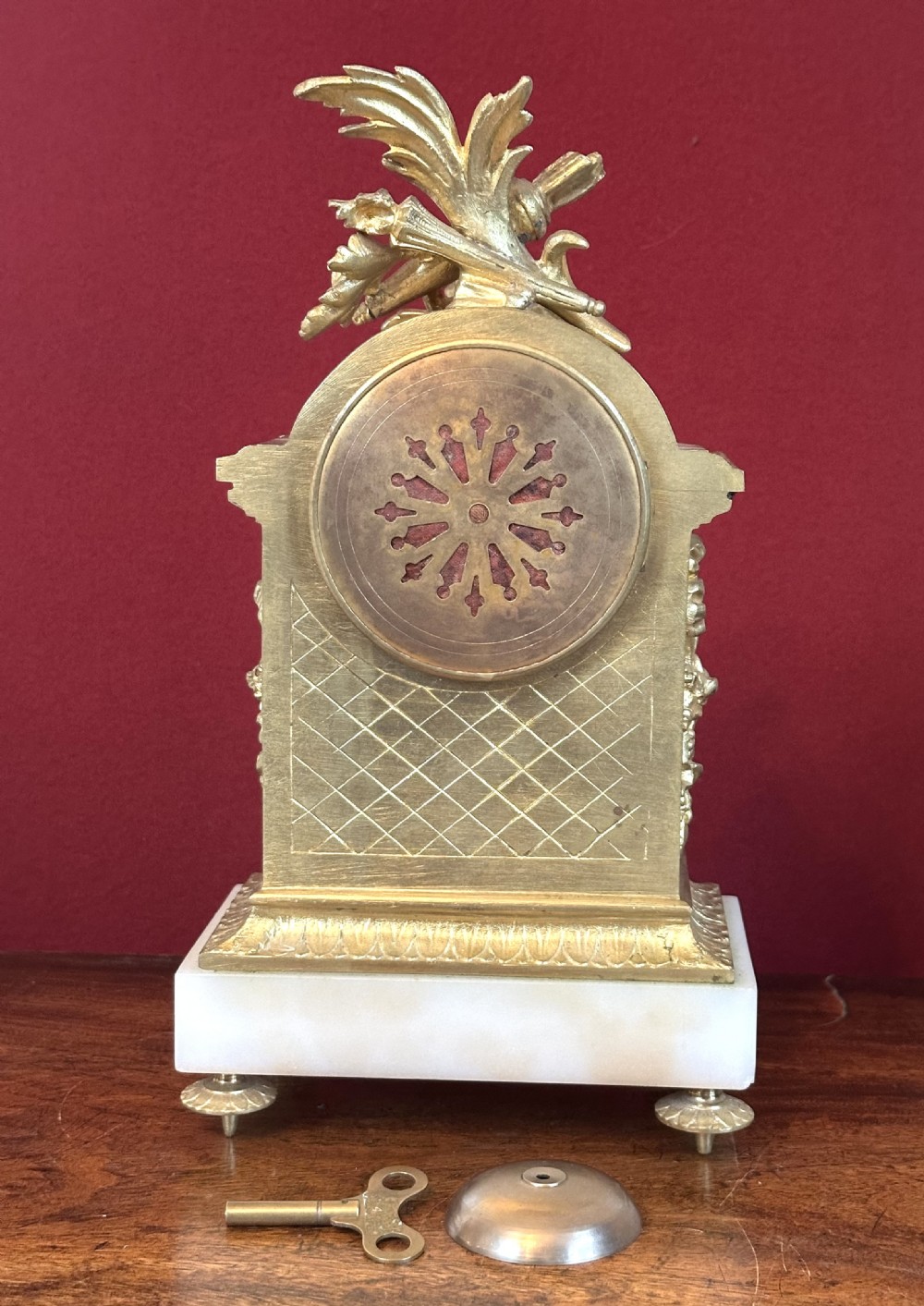 An antique late 19th-century French gilt bronze and white alabaster mantel clock featuring a hand-painted enamel dial, floral swags, and a quiver motif on top. View VI