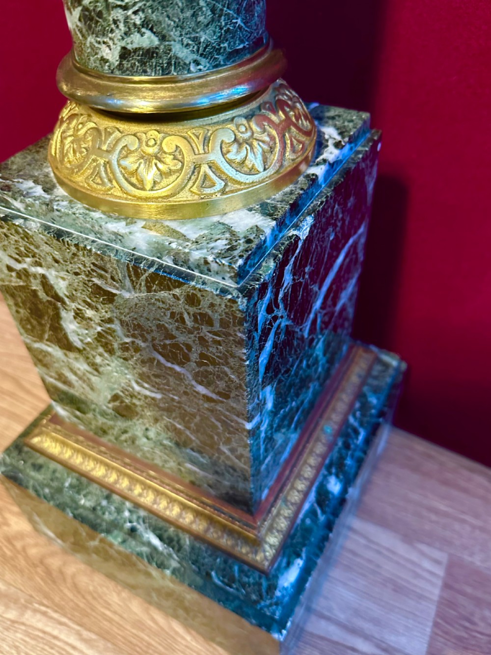A tall dark green veined marble column pedestal featuring a square top, gilt bronze Corinthian capital, cylindrical shaft, and a stepped square base. View IV