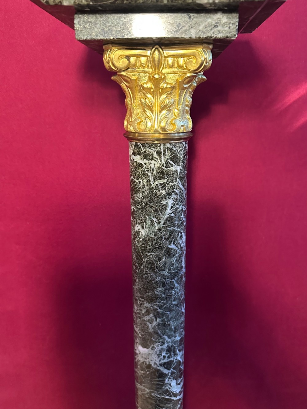 A tall dark green veined marble column pedestal featuring a square top, gilt bronze Corinthian capital, cylindrical shaft, and a stepped square base. View VII
