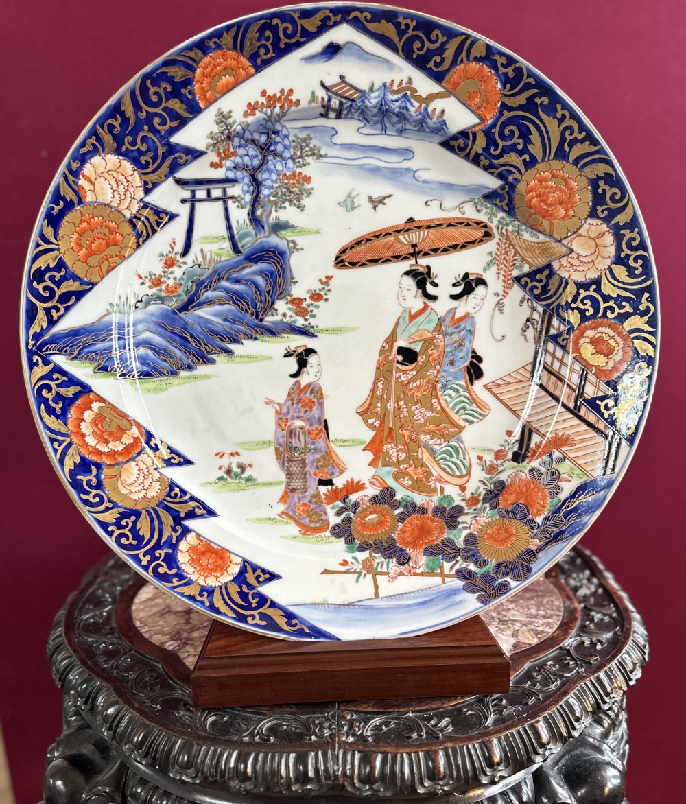 A large circular Japanese Imari porcelain charger featuring hand-painted figures in a landscape surrounded by an ornate cobalt blue and orange floral border. View II