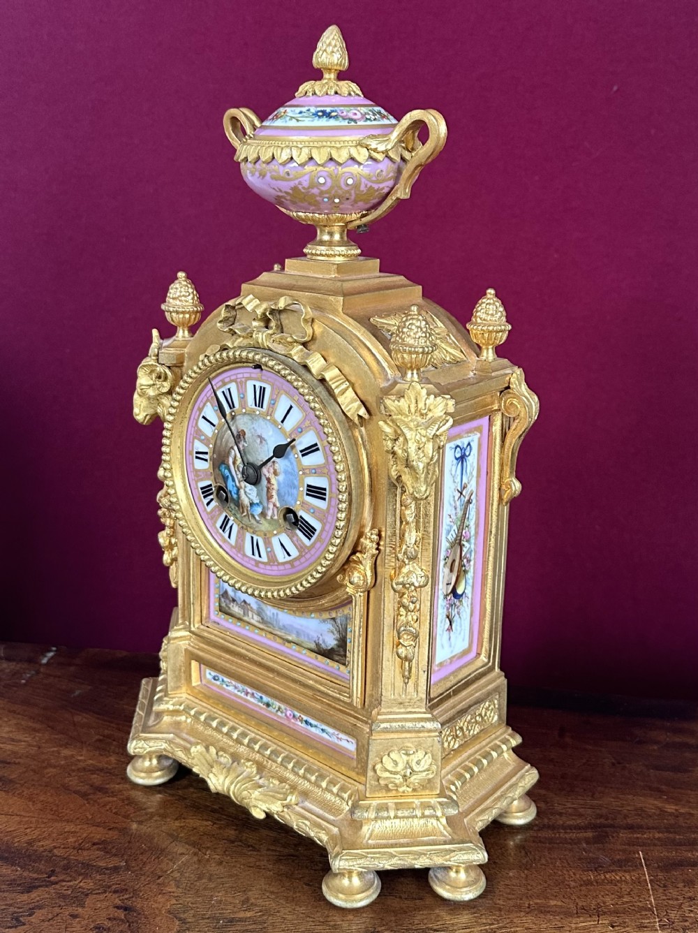 A late 19th-century French gilt bronze mantel clock featuring pink hand-painted porcelain panels and an urn finial.