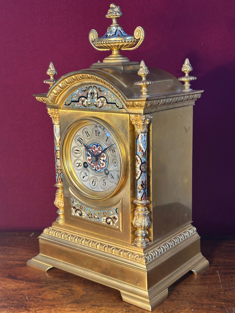 A late 19th-century French gilt-bronze mantel clock decorated with multicoloured champleve enamel scrollwork, columns, and an urn finial.